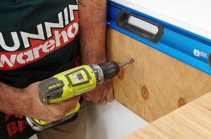 Person drilling thin piece of timber into wall.