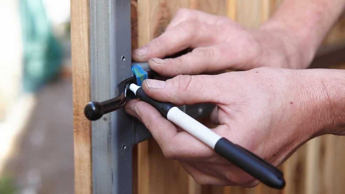 Person using permanent marker to mark screw points in gate latch.