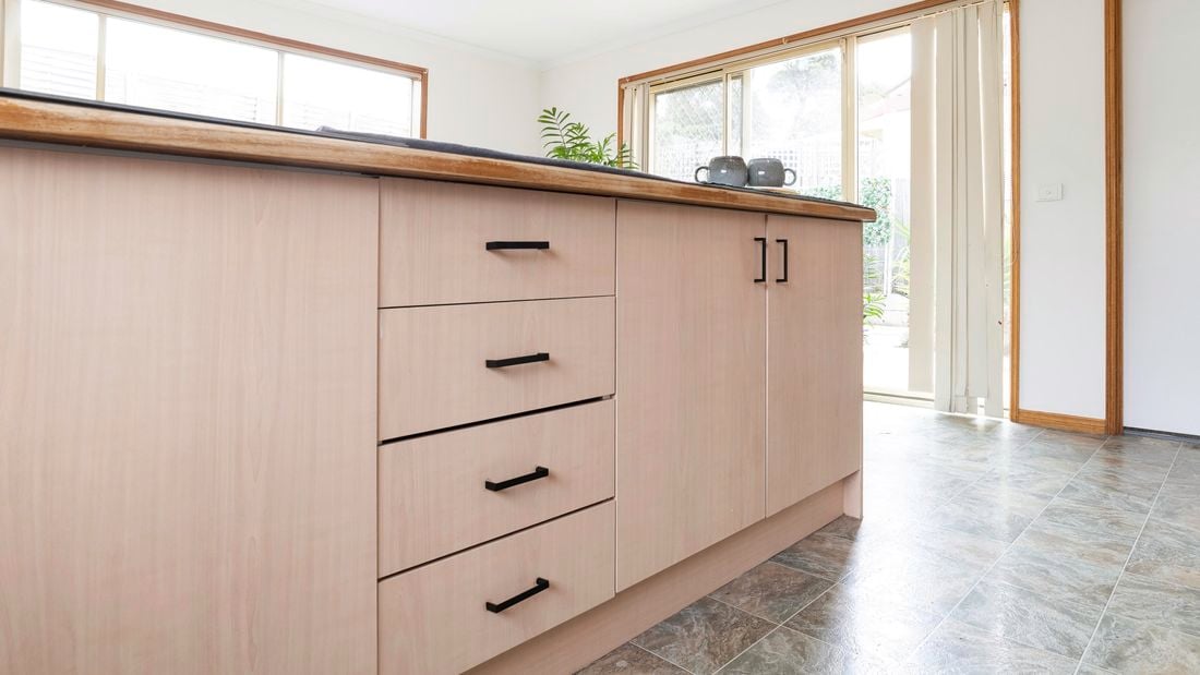 Closeup of wood finish kitchen cabinets with new black handles attached, as part of a white and wooden themed dining area