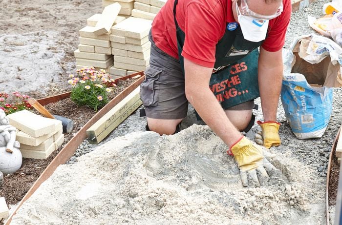 A person spreading sand by hand on the base of a pathway