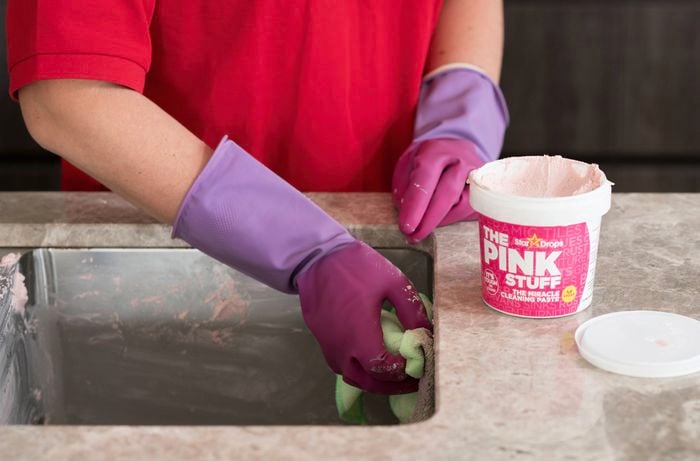 A gloved hand is applying the pink stuff miracle cleaning paste using a microfiber cloth.