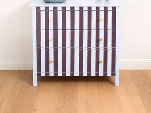 Small cabinet with vertical burgundy and white stripes, photographed front-on against a plain wall.