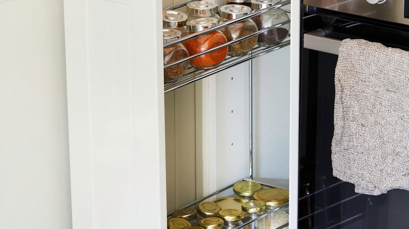 Open white cupboard containing pull out baskets used as a spice rack