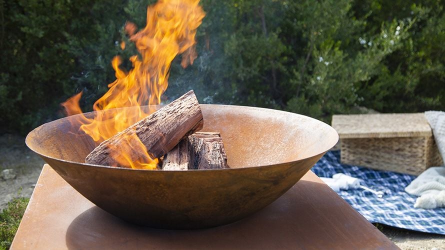 A lit brazier on a raised platform in front of a rug and picnic basket