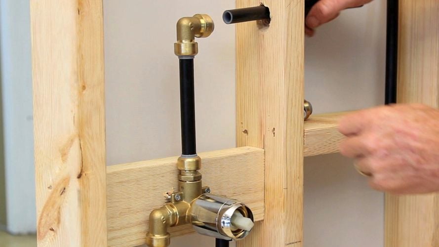 A person connecting a black pipe to a copper elbow.