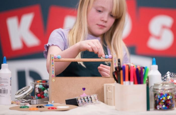 In a Bunnings DIY workshop, a kid is decorating a tool caddy with sequins and pompoms.