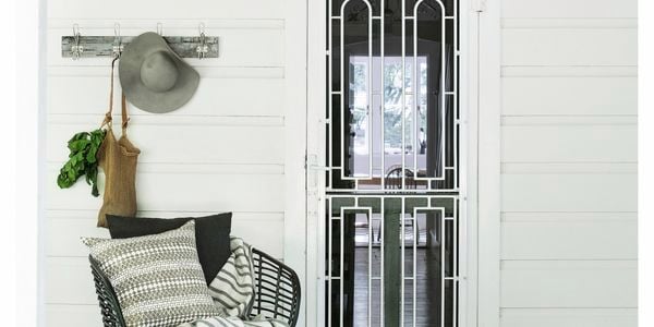 Screen door on a white house porch with a cushioned chair to the left of the door.
