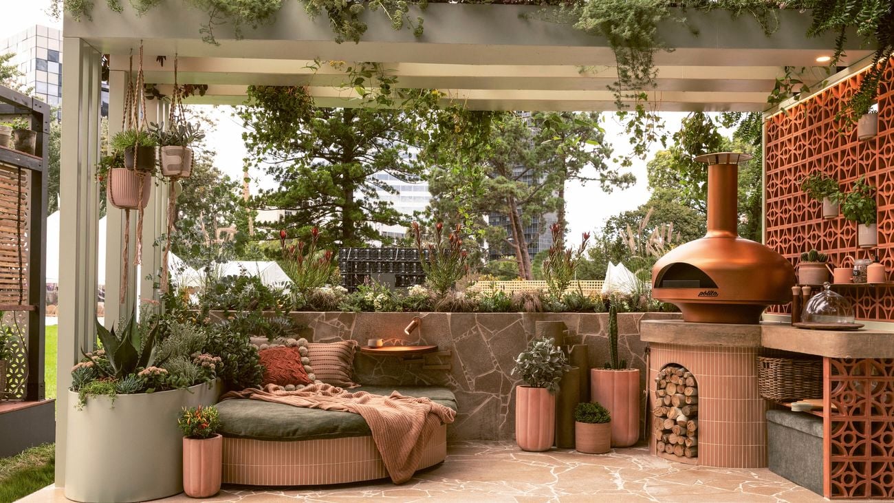 Cosy outdoor room with a built-in pizza oven and seating, a raised planter, pots and hanging plants.