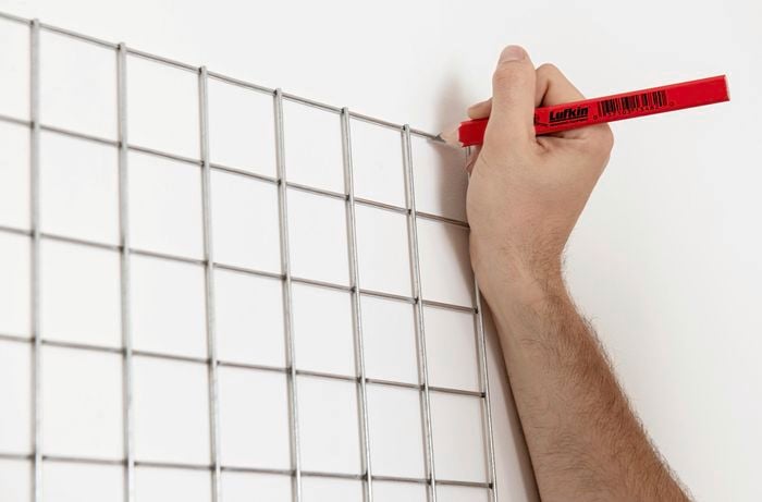 A pencil being used to mark out the position of a mesh grid on a wall
