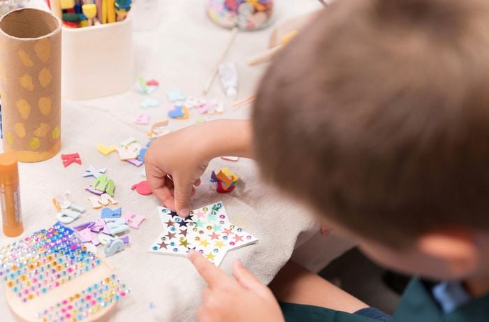 A kid is decorating a coaster with paint markers, and stickers.