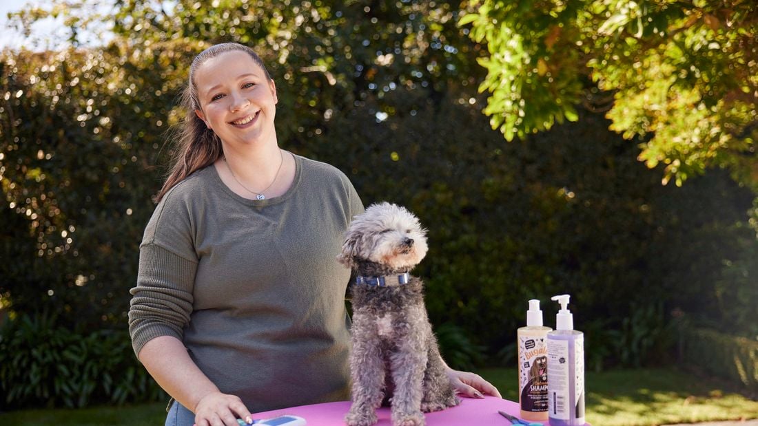 The lady is standing with her dog ready to get groomed 