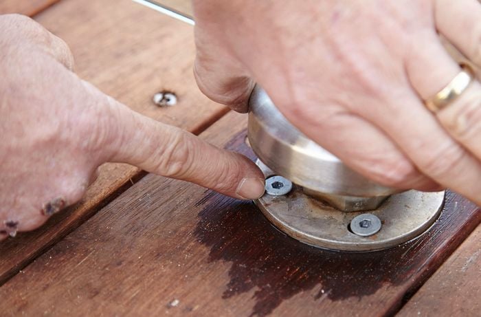 The base of a glass pool fence with a hand pointing to the bolts securing it to the deck below