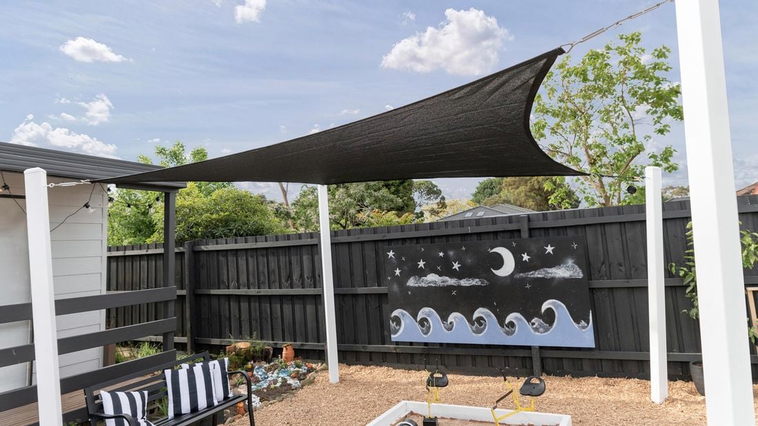 An installed black shade sail over a kindergarten sandpit