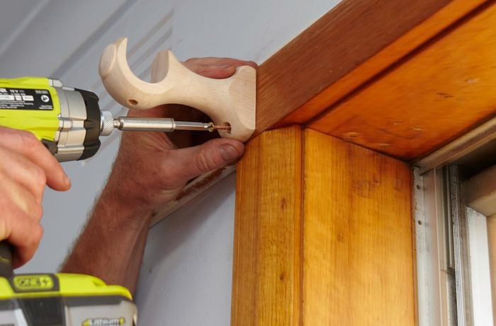 Person drilling curtain rod hanger into window frame.