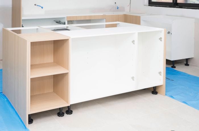 Kitchen cabinets are carefully placed on protective blue sheets to install the kitchen island.