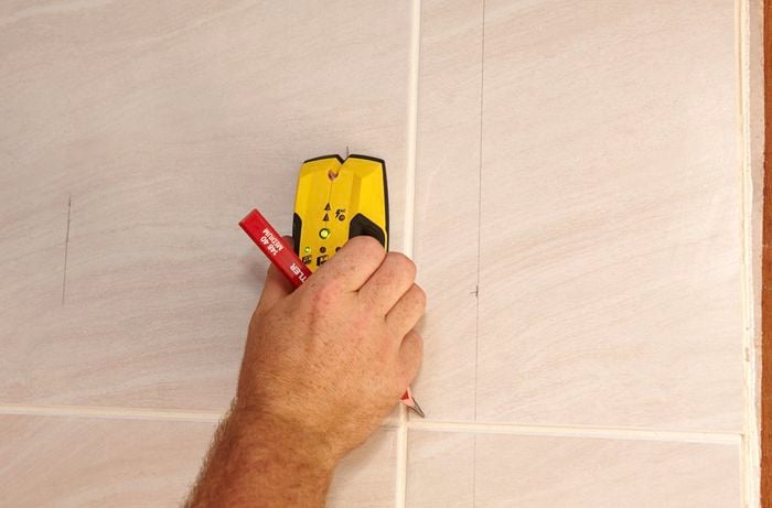 A person using a stud finder on a tiled wall