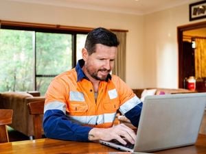 A man in hi-vis working on a laptop placed on a dining table inside a home