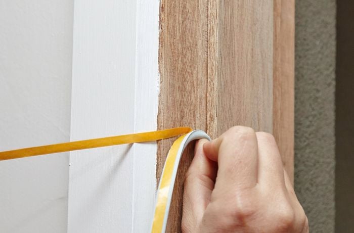 A person applying a self-adhesive draft seal around a door frame