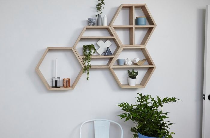 A honeycomb wall shelf array mounted on a white wall with a pot plant below it