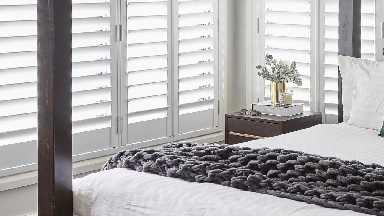 Bedroom with full length, white shutters covering windows.