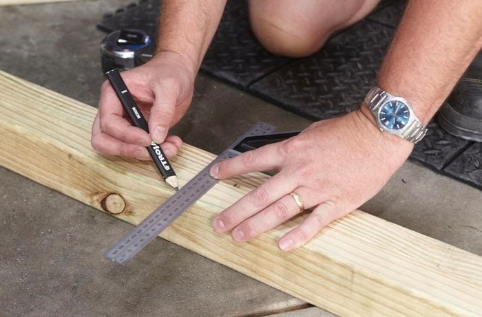 Person using pencil and steel ruler to mark piece of timber.