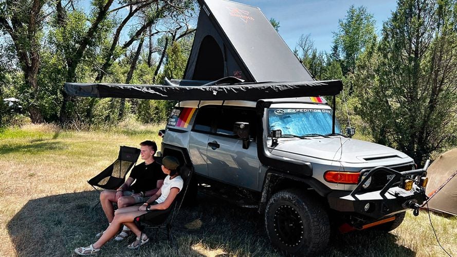 two people sitting under a side sail that is attached to their car