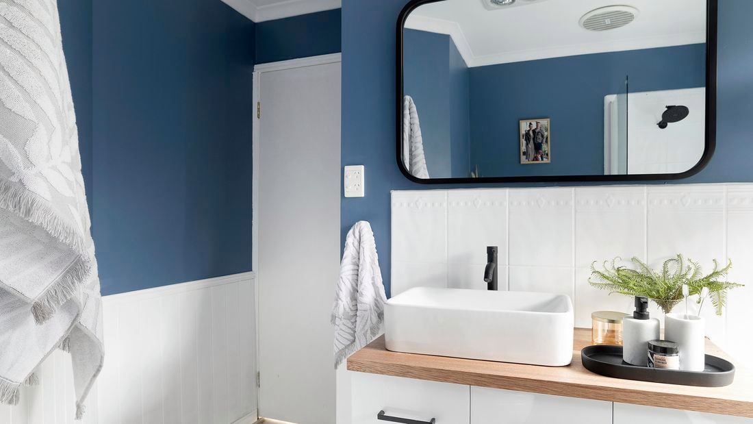 Blue bathroom with white sink and black framed mirror.