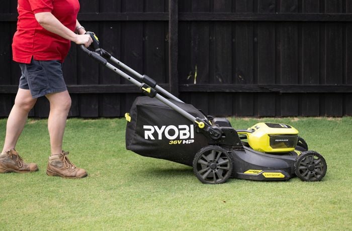A person is using a brushless cordless lawn mower to mow the lawn. 
