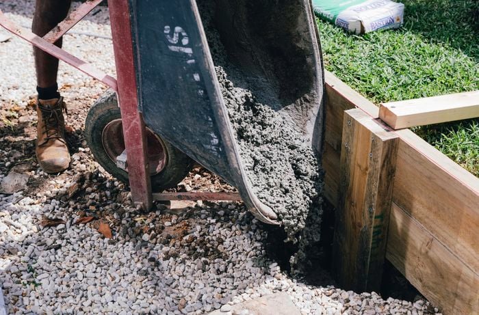Concrete being poured into a posthole to secure a retaining wall's vertical post