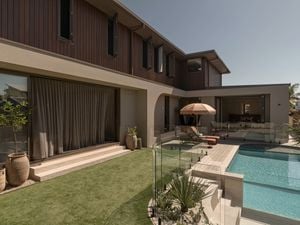 Contemporary two-storey house with timber cladding and rendered walls overlooking a backyard with a glass-fenced swimming pool, patio seating, and landscaped garden.