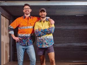 TIACS co-founder Ed Ross stands smiling and pointing to the slogan on the back of Dan Ross brightly coloured shirt