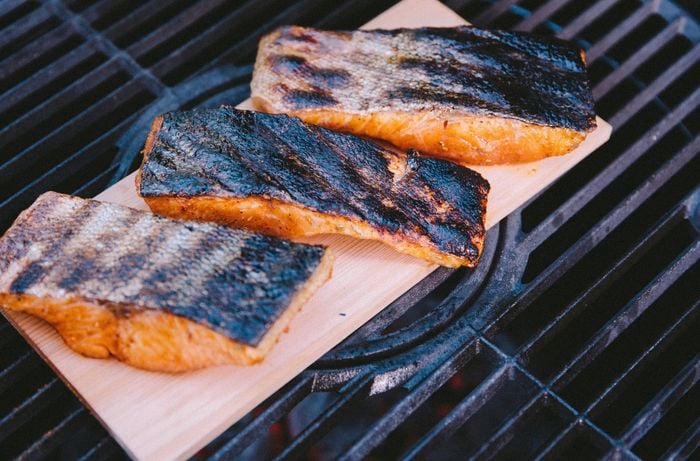 Fillets of salmon with charred skin on a grilling plank resting on a BBQ grill