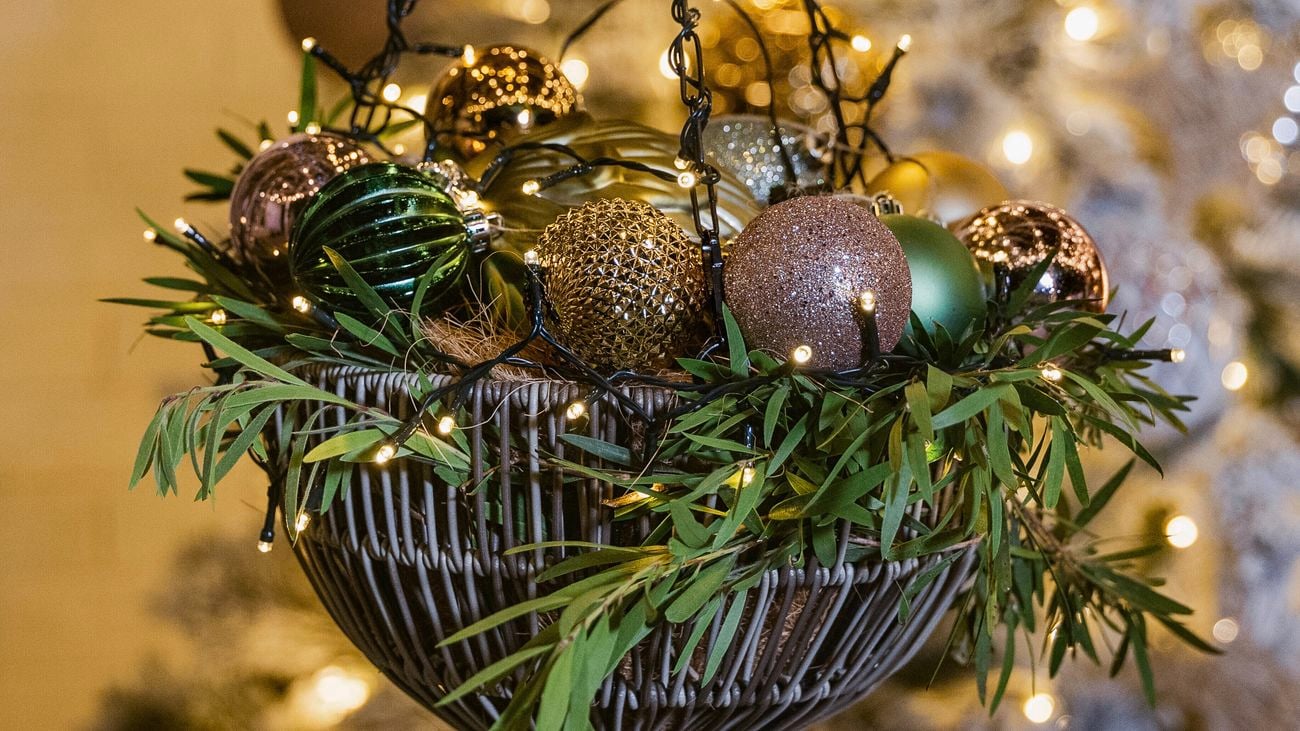 Hanging basket with greenery, baubles, and fairy lights in front of a lit Christmas tree.