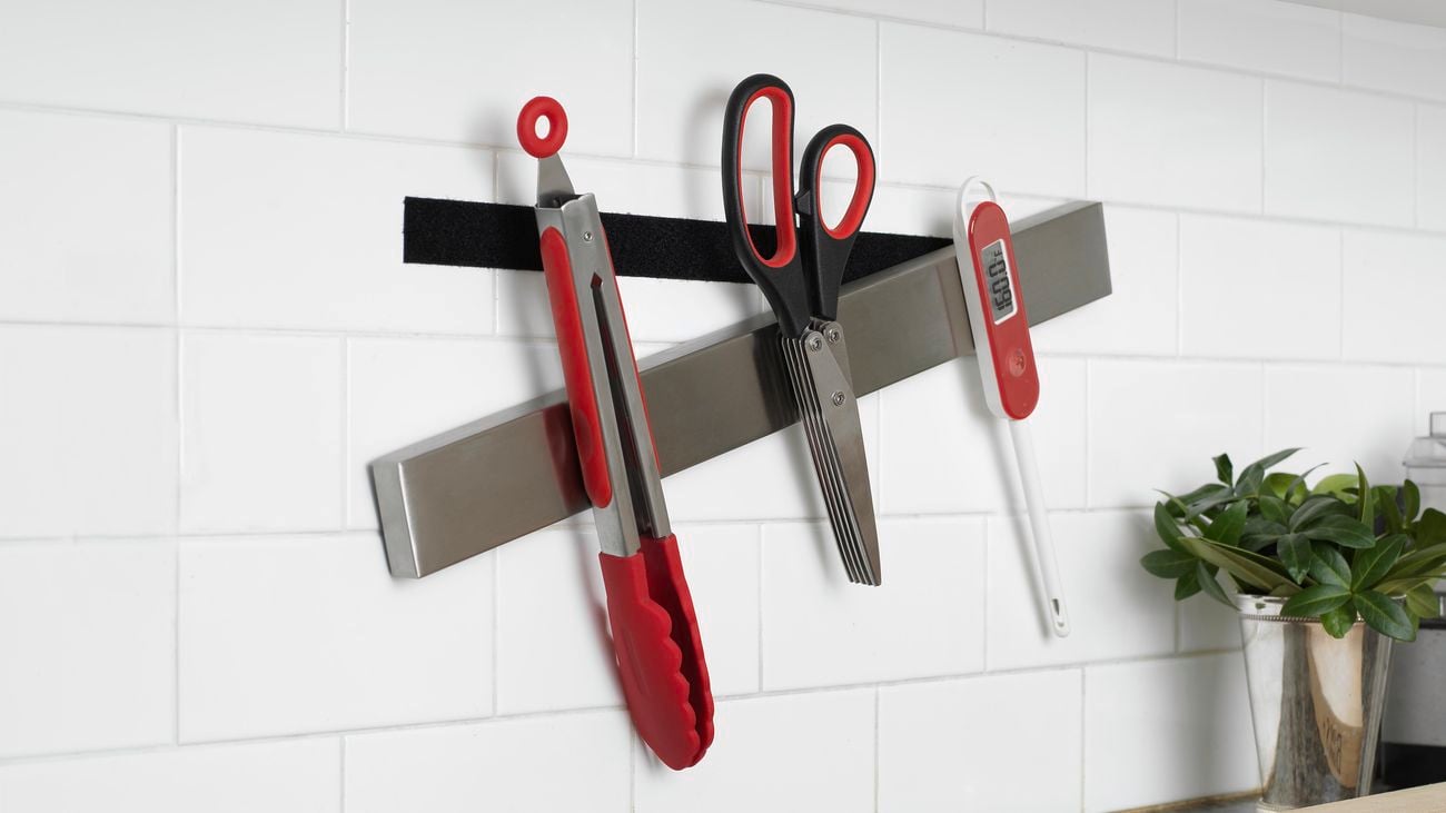 Tongs, scissors and a meat thermometer attach to a metal, magnetic strip, stuck on wall with VELCRO®