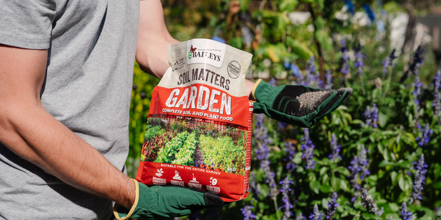 Person spreading soil matters on a garden bed.