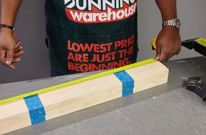 A person measuring lengths of pine timber taped together
