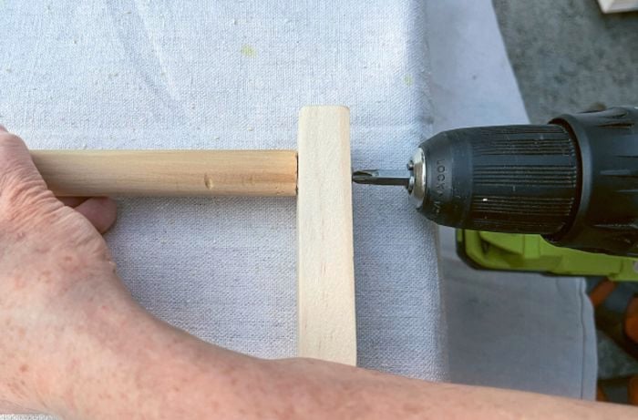 A hand holds a piece of dowel against a piece of pine as a screw is driven into the pine.