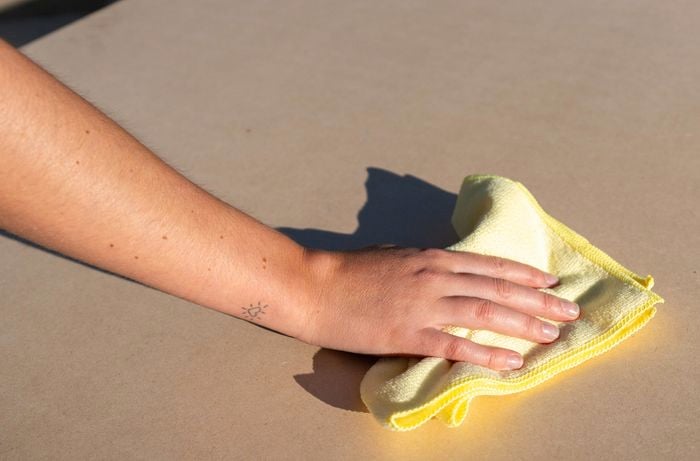 A person is wiping an MDF panel with a clean cloth to remove dust and prepare the surface.