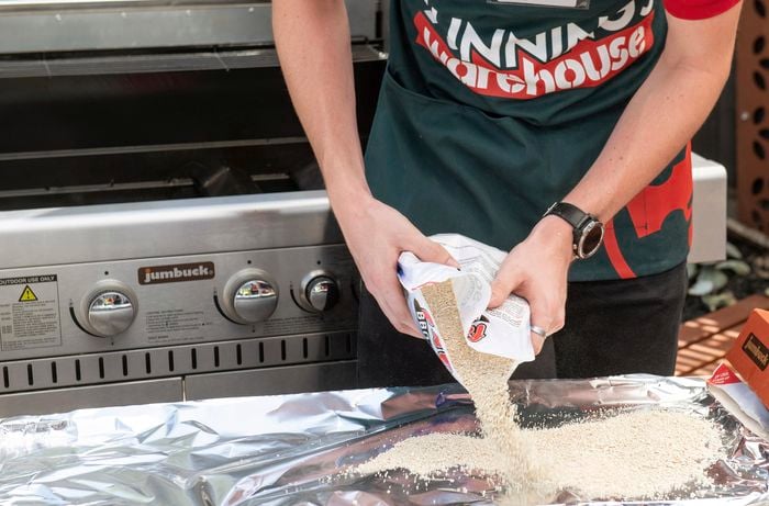 A person sprinkling Fat-sorb on a BBQ drip tray lined with aluminium foil