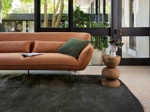 Burnt orange lounge, timber side table all sitting on a thick charcoal rug in living room.