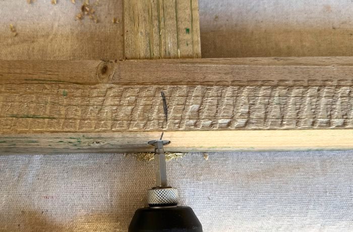 Close up of a drill driving a screw into a timber frame.