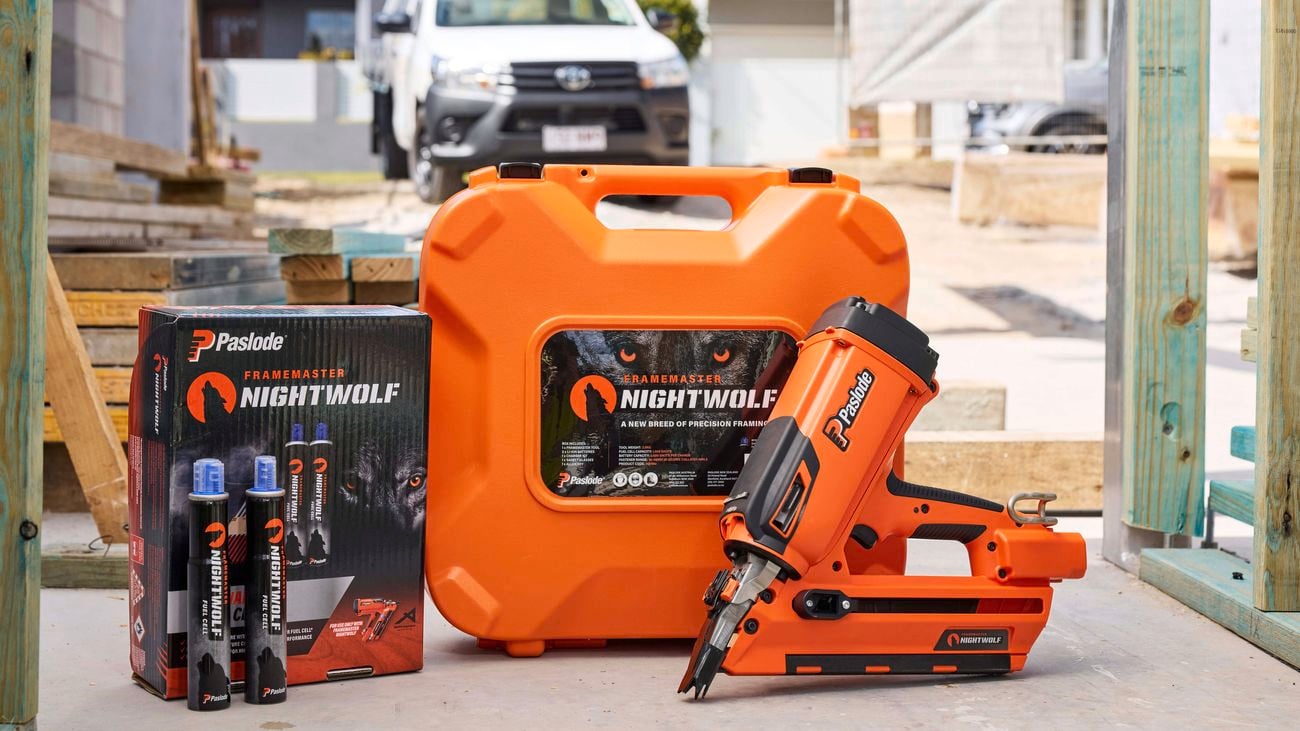 A product image of the Paslode FrameMaster NightWolf, nails and fuel canisters with a building site as the backdrop