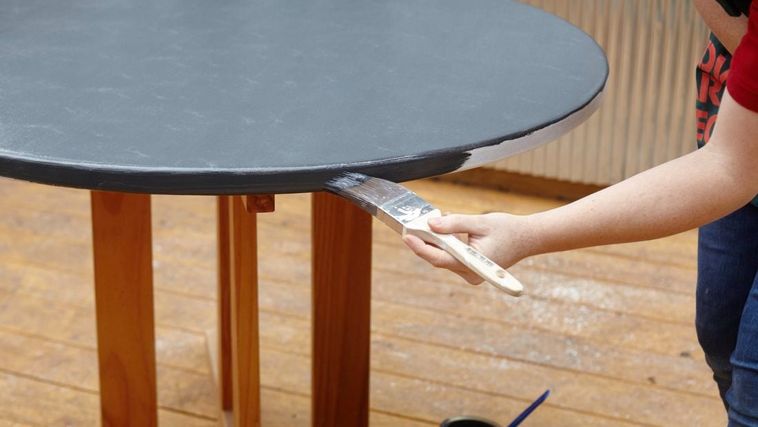 A Bunnings team member painting the edge of a table in Bunnings teal