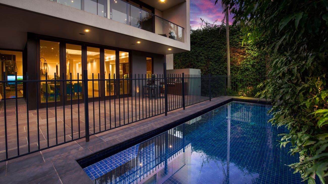 Black fence sit beside a pool in backyard of modern house 