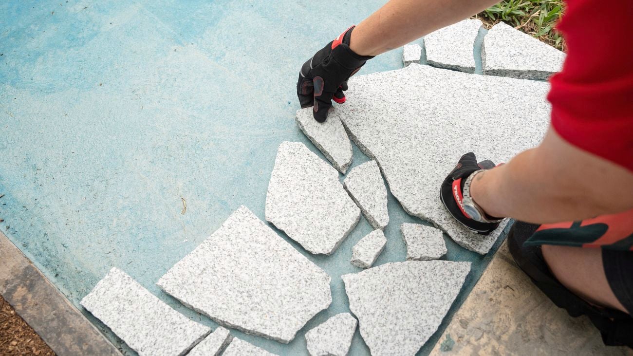 A person laying pavers on concrete path.