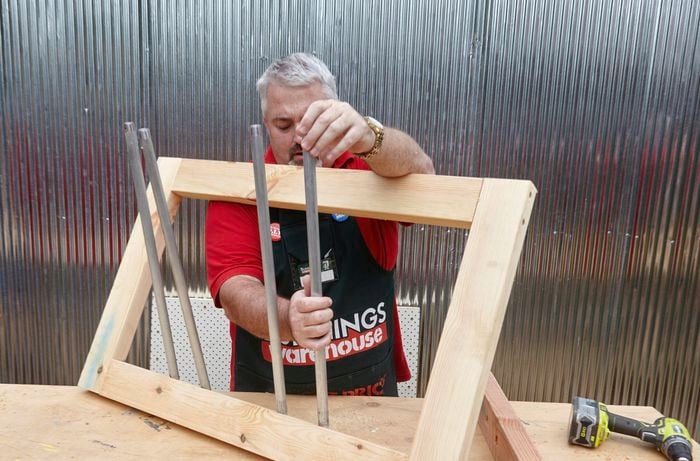A person inserting galvanised pipes into holes in a timber frame