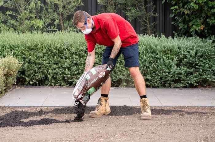 A Bunnings Team Member is spreading lawn soil from a bag onto the ground to help the turf grow strong and healthy.