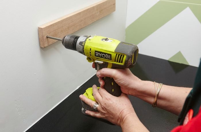 A person attaching a timber knife rack to a wall using a cordless driver
