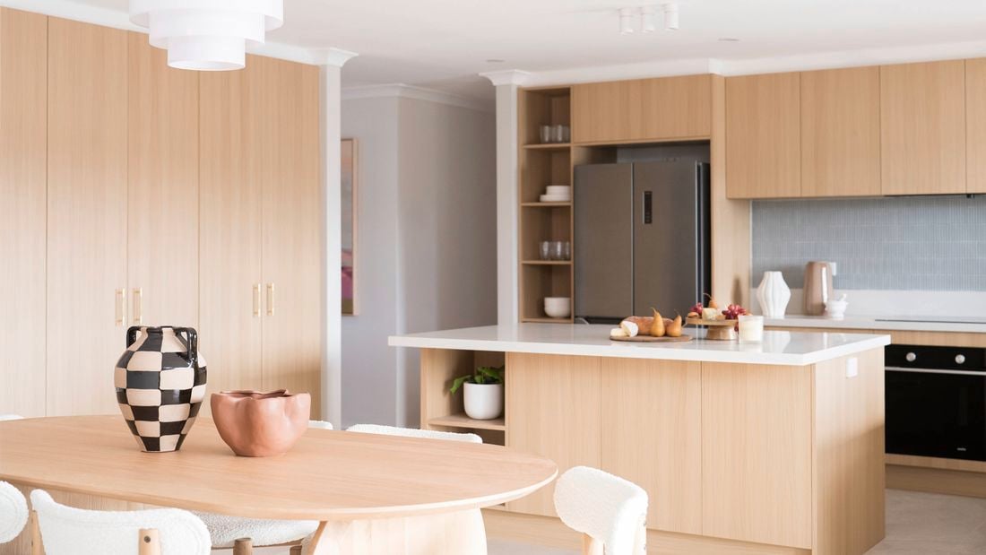 A modern kitchen features light wood cabinetry, a large island with a white benchtop, creating a clean and stylish space.