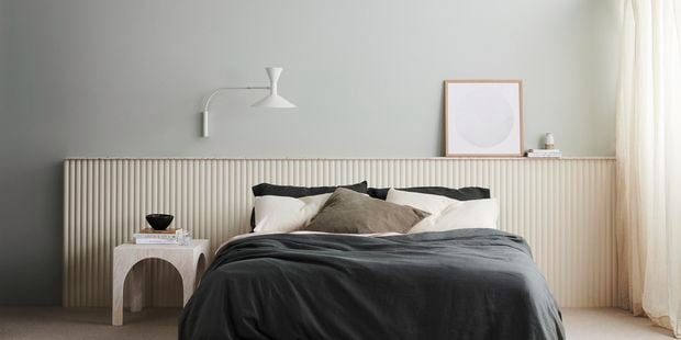 Bedroom with bed, scattered pillows, side table with books, mounted lamp and print. Demi Round 40 design.